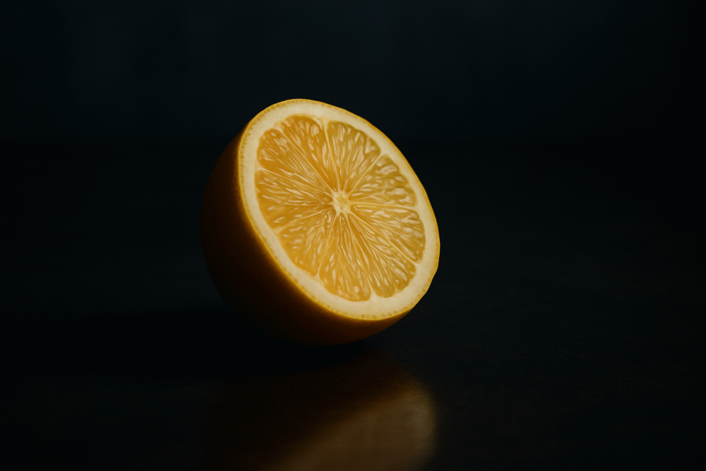 Lemonading. A halved lemon resting on a dark reflective surface with soft directional lighting, symbolizing emotional resilience and growth emerging from hardship.